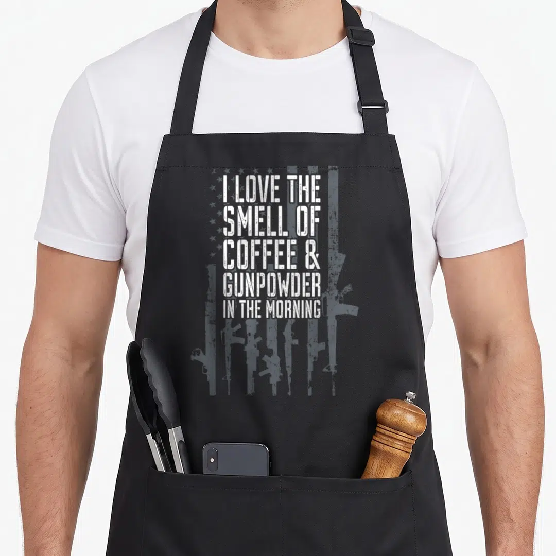 Smell coffee apron - I LOVE THE SMELL OF COFFEE & GUNPOWDER IN THE MORNING text over distressed rifles and flag pattern — shown on a black cotton canvas apron against a white background