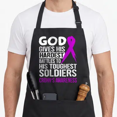 Touchest crohns awareness apron - Purple awareness ribbon over stacked white and black text reading God Gives — shown on a black cotton canvas apron against a white background