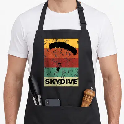 Instructor skydiving apron - Retro skydiver silhouette over yellow orange red green stripes with SKYDIVE text on cream — shown on a black cotton canvas apron against a white background