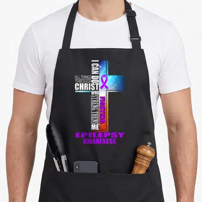 Funny warrior epilepsy awareness apron - 3D cross with ALL THINGS THROUGH CHRIST text and purple epilepsy ribbon — shown on a black cotton canvas apron against a white background