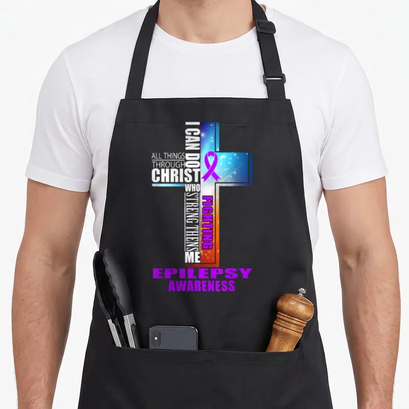 Funny warrior epilepsy awareness apron - 3D cross with ALL THINGS THROUGH CHRIST text and purple epilepsy ribbon — shown on a black cotton canvas apron against a white background