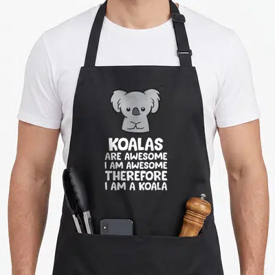 Koalas therefore apron - Cartoon grey koala above five lines of white text reading KOALAS ARE AWESOME I AM AWESOME — shown on a black cotton canvas apron against a white background
