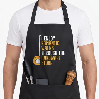 Store handyman apron - Yellow tape measure next to stacked text reading I enjoy romantic walks through the hardware — shown on a black cotton canvas apron against a white background