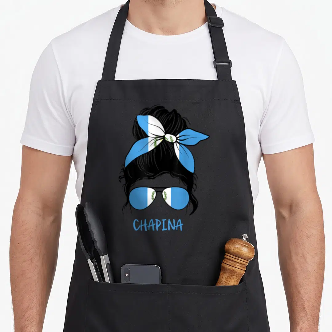 Chapina pride apron - Stylized woman with Guatemalan flag bun, sunglasses, and CHAPINA text in blue, white, green — shown on a black cotton canvas apron against a white background