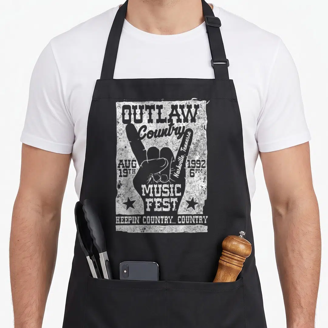 Outlaw cook's country aprons - White distressed hand gesture with OUTLAW Country 1992 Nashville text and stars — shown on a black cotton canvas apron against a white background