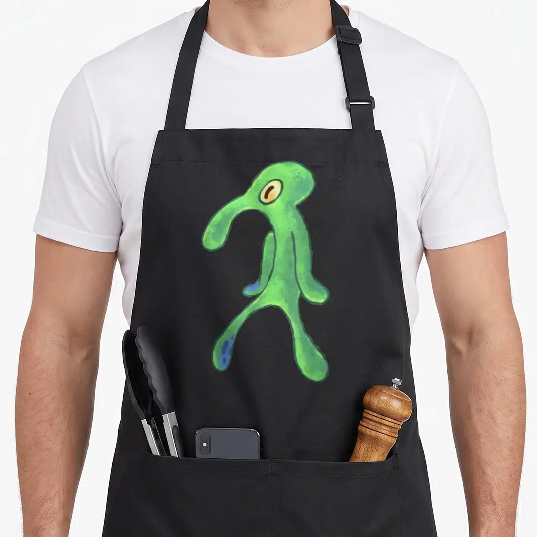 Bold general apron - Green cartoon alien creature with blue spots and single eye — shown on a black cotton canvas apron against a white background