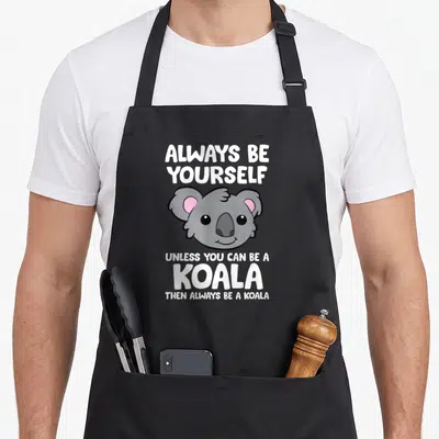 Alway koala apron - Cartoon grey koala head with pink ears and white stacked text — shown on a black cotton canvas apron against a white background