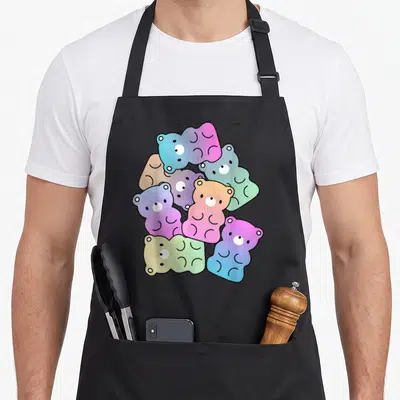 Rainbow bear apron - Seven overlapping gummy bears in pink, blue, green, yellow, and purple gradients — shown on a black cotton canvas apron against a white background