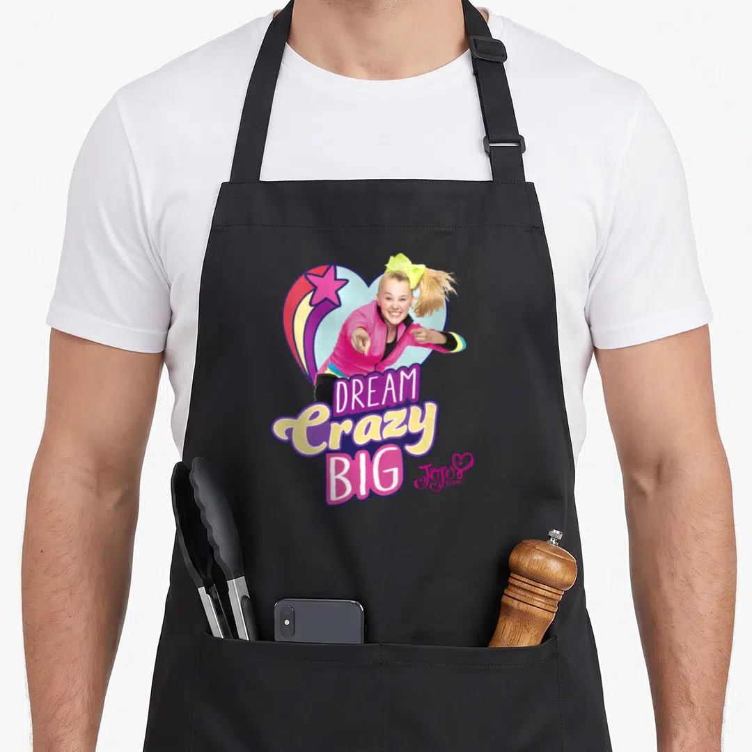 Dream shooting apron - Cartoon girl pointing with DREAM Crazy BIG text and shooting star heart — shown on a black cotton canvas apron against a white background