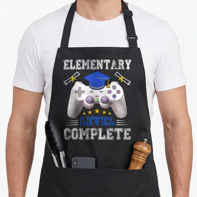 Elementary class funny apron - Game controller with blue graduation cap, two diplomas, five stars, and elementary level — shown on a black cotton canvas apron against a white background