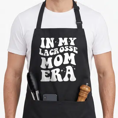 Era lacrosse mom apron - White stacked text IN MY LACROSSE MOM ERA with small stars — shown on a black cotton canvas apron against a white background