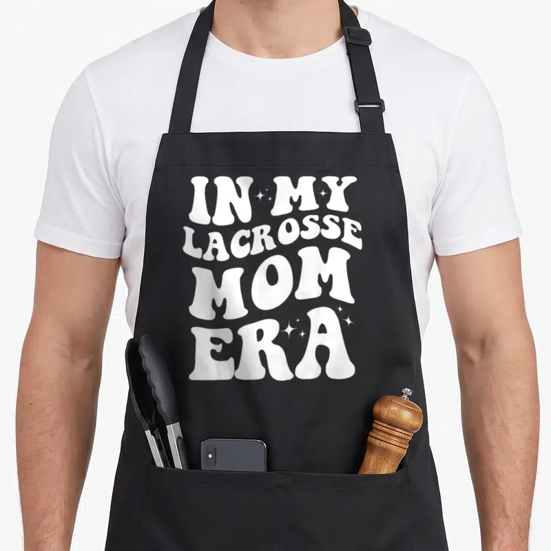Era lacrosse mom apron - White stacked text IN MY LACROSSE MOM ERA with small stars — shown on a black cotton canvas apron against a white background