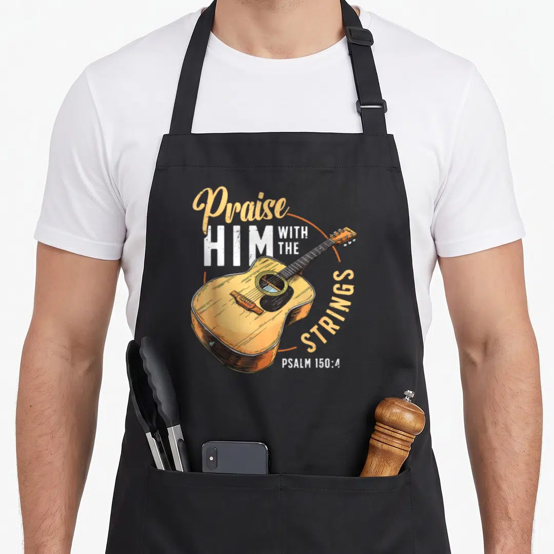 String bible christian apron - Retro acoustic guitar with Praise HIM WITH THE STRINGS text in orange and white — shown on a black cotton canvas apron against a white background