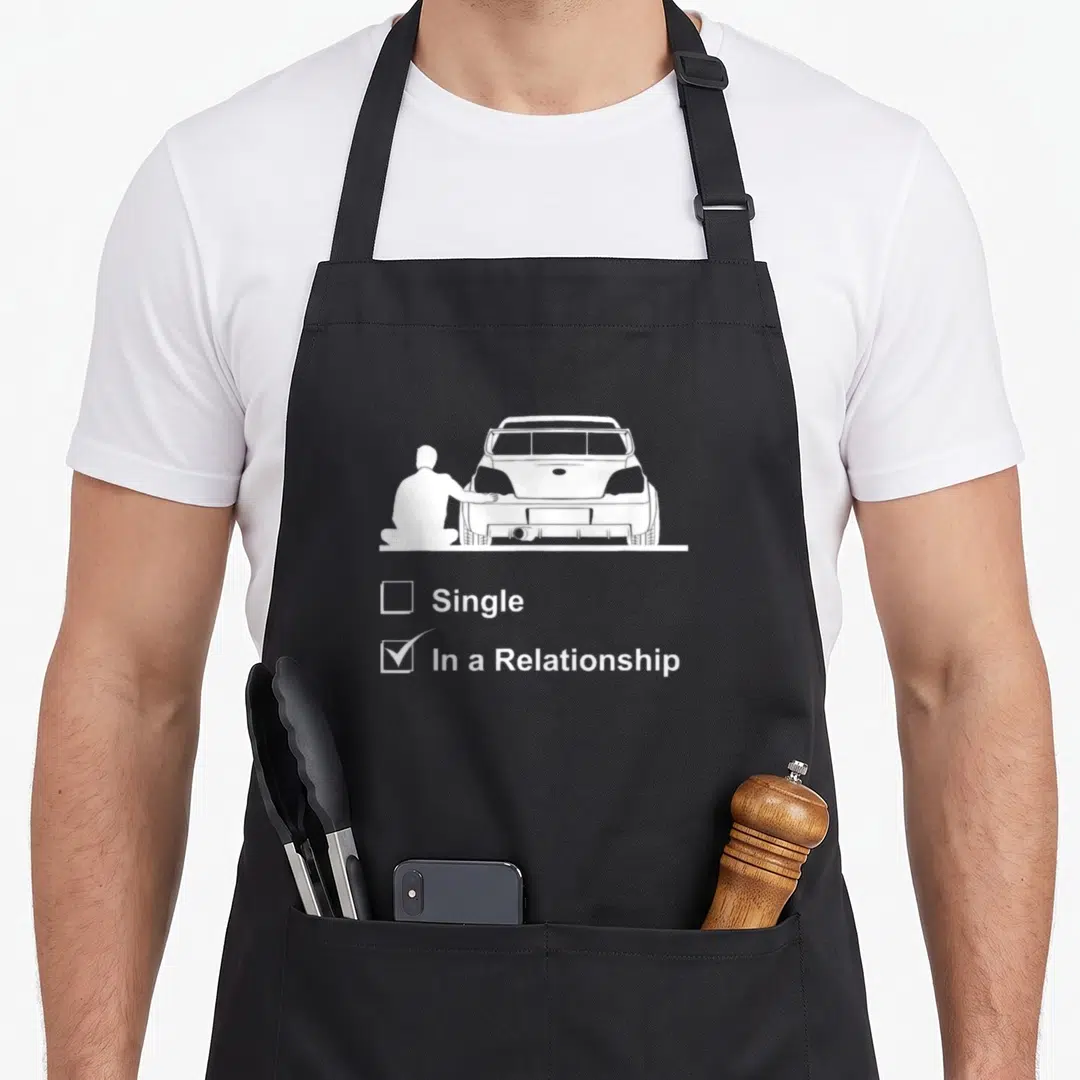 Culture design imports vintage apron - White graphic of man kneeling by car rear with single and in a relationship — shown on a black cotton canvas apron against a white background
