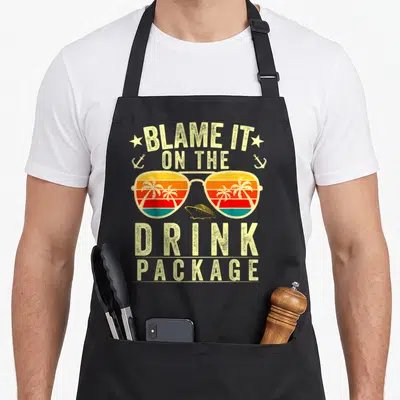 Blame cruising apron - Retro sunglasses with sunset palm trees and cruise ship. Text reads blame it on the drink package — shown on a black cotton canvas apron against a white background
