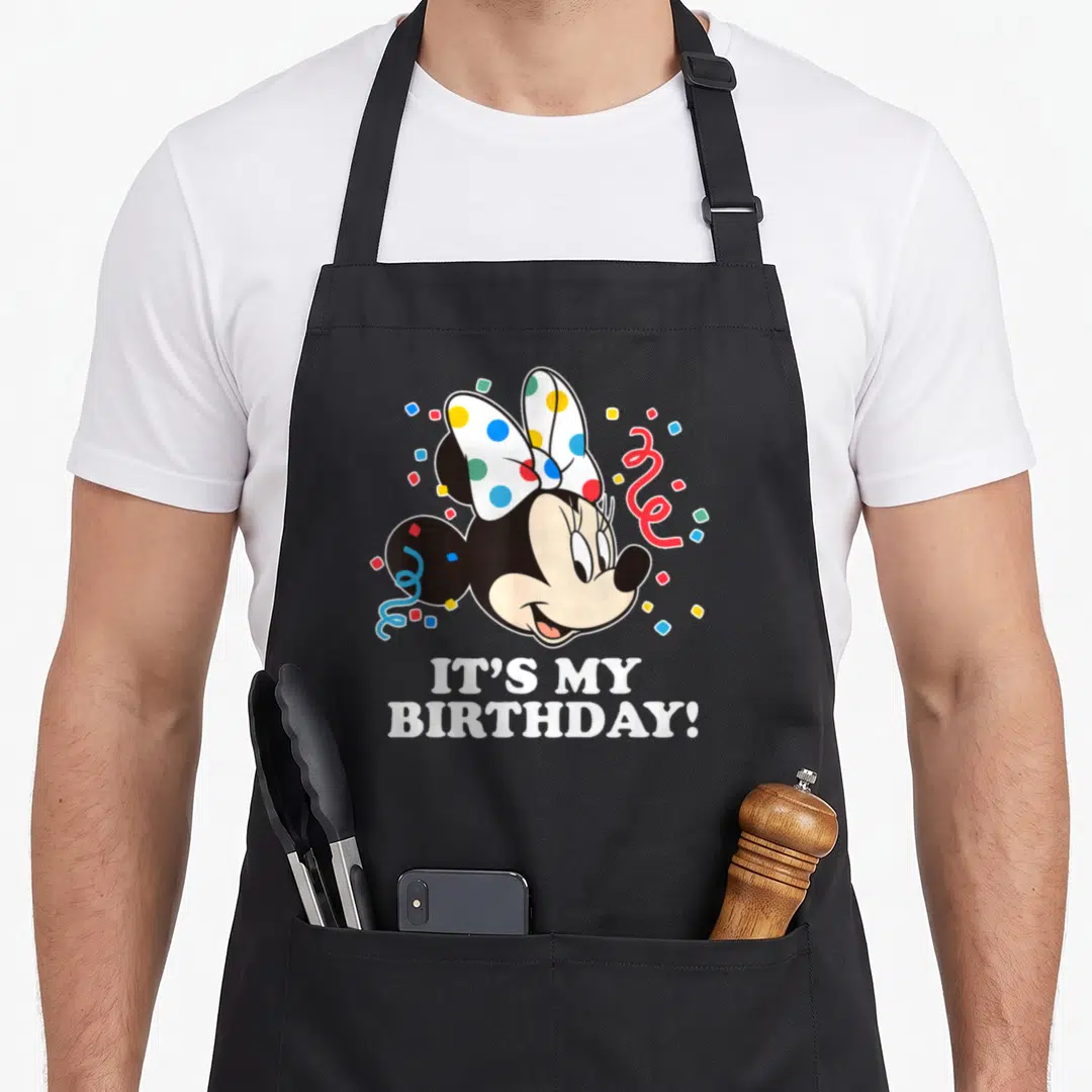 Born day apron - Minnie Mouse head with IT'S MY BIRTHDAY! text and colorful confetti — shown on a black cotton canvas apron against a white background