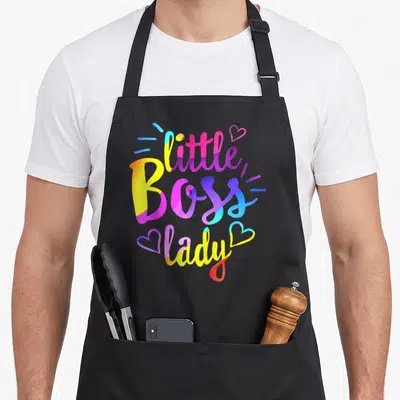 Ittle bbq boss apron - Stacked colorful text reading little Boss lady with two hearts and accent lines — shown on a black cotton canvas apron against a white background