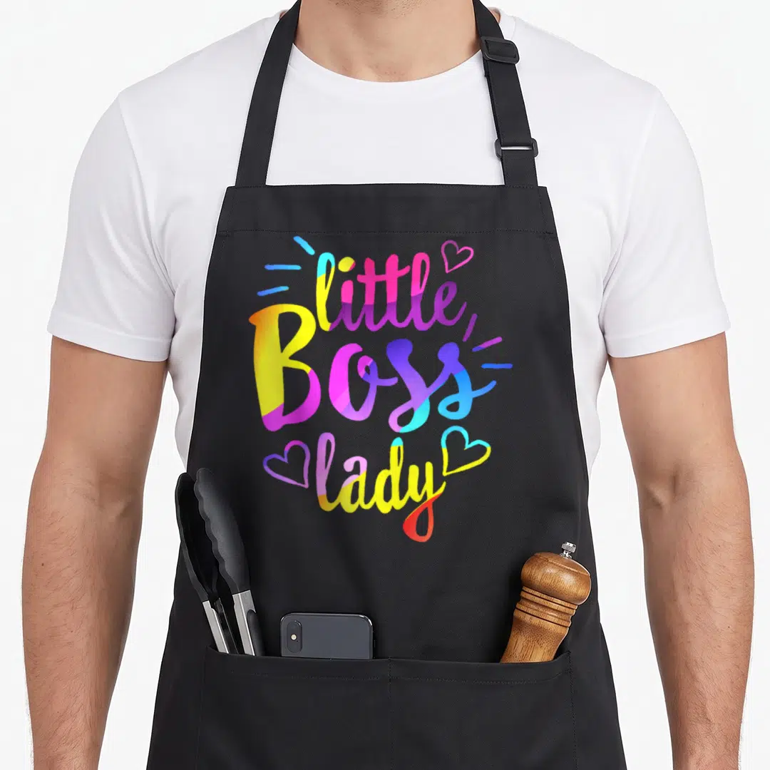Ittle bbq boss apron - Stacked colorful text reading little Boss lady with two hearts and accent lines — shown on a black cotton canvas apron against a white background