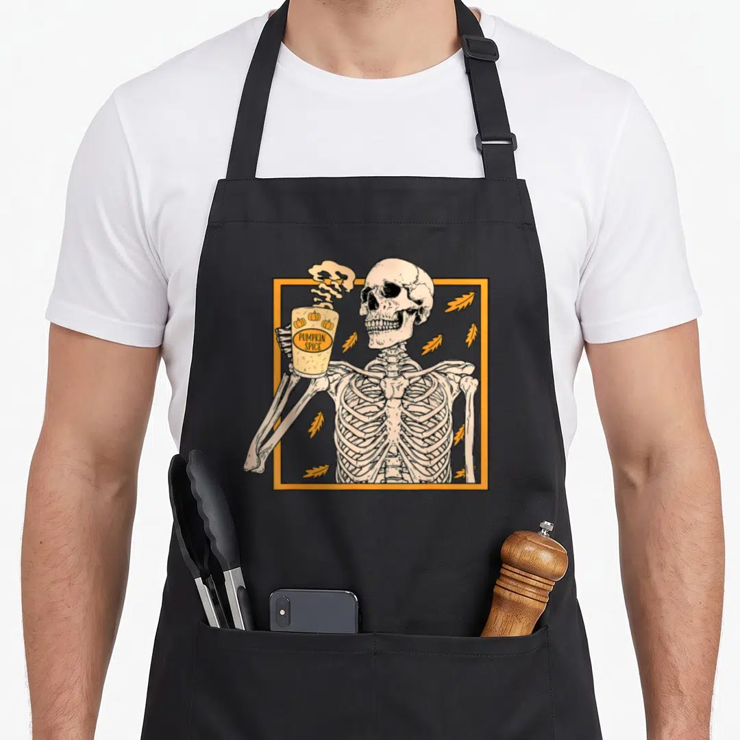 Spice halloween apron - Skeleton holding pumpkin spice cup inside orange frame with scattered leaves — shown on a black cotton canvas apron against a white background