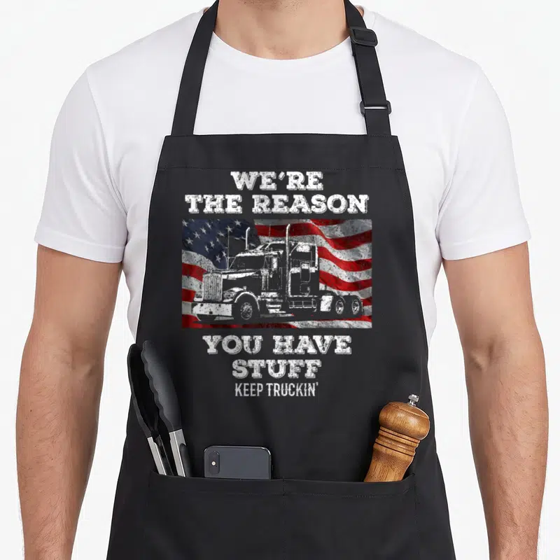 Reason semi truck apron - Semi-truck silhouette over waving USA flag with We're The Reason You Have Stuff Keep Truckin' — shown on a black cotton canvas apron against a white background