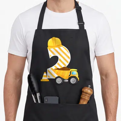 Construction dump truck apron - Striped number 2 in a hard hat with a yellow dump truck and traffic cone — shown on a black cotton canvas apron against a white background