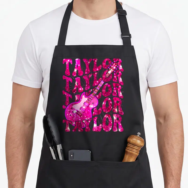 Vintage taylor 80s apron - Pink glitter electric guitar overlaid on five stacked rows of TAYLOR text — shown on a black cotton canvas apron against a white background