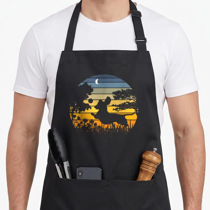 Dog wiener apron - Retro dachshund jumping silhouette against striped sunset circle with moon and garden flora — shown on a black cotton canvas apron against a white background