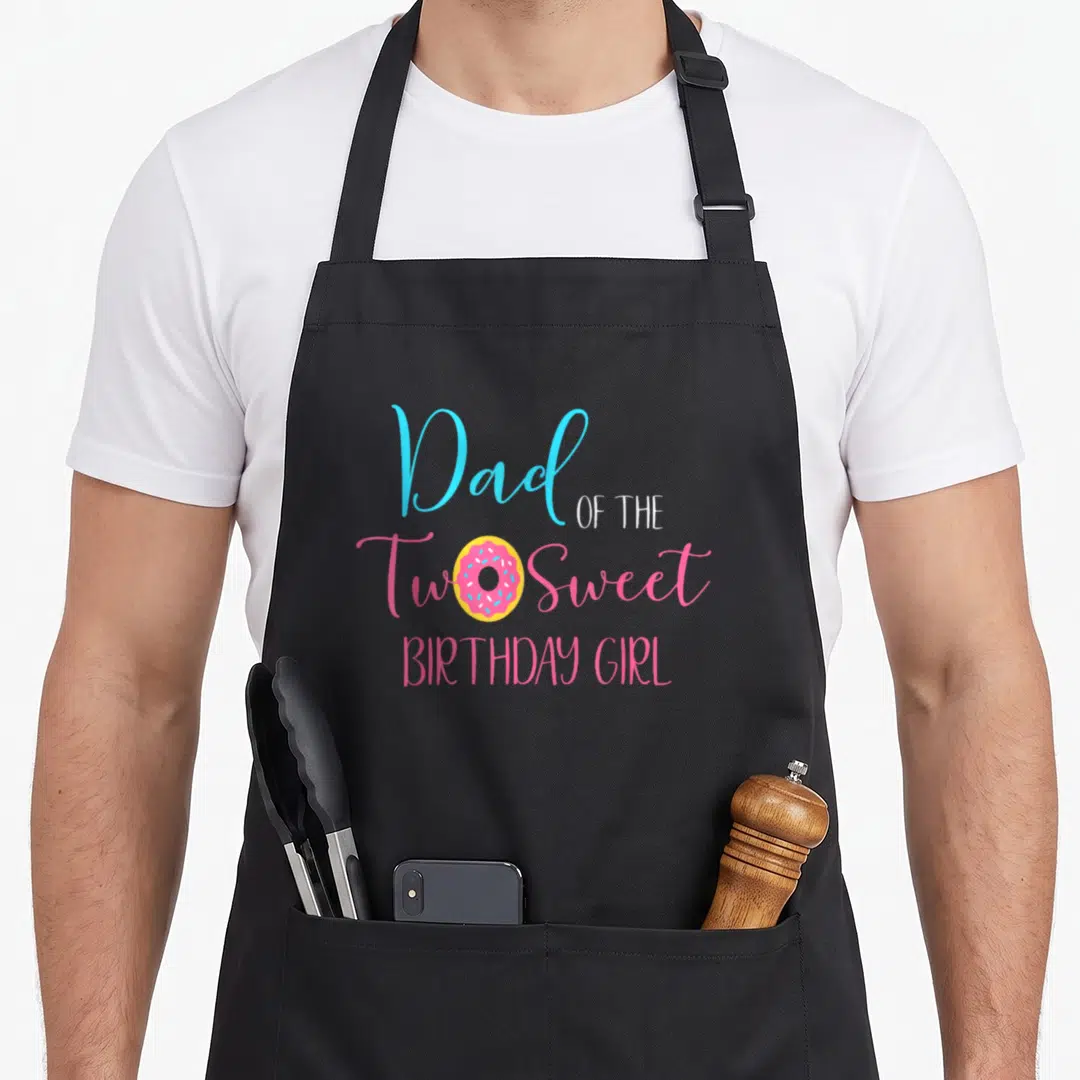 Cute sweet birthday apron - Dad OF THE Two Sweet BIRTHDAY GIRL text with pink donut replacing the O in Two — shown on a black cotton canvas apron against a white background