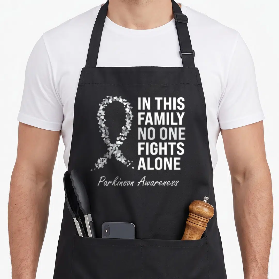 Parkinson awareness ribbon apron - White and grey heart ribbon next to In This Family No One Fights Alone text — shown on a black cotton canvas apron against a white background