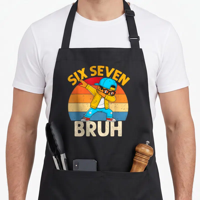 Dabbing number meme apron - Cartoon boy dabbing under arched Six Seven text and above Bruh on striped sun — shown on a black cotton canvas apron against a white background
