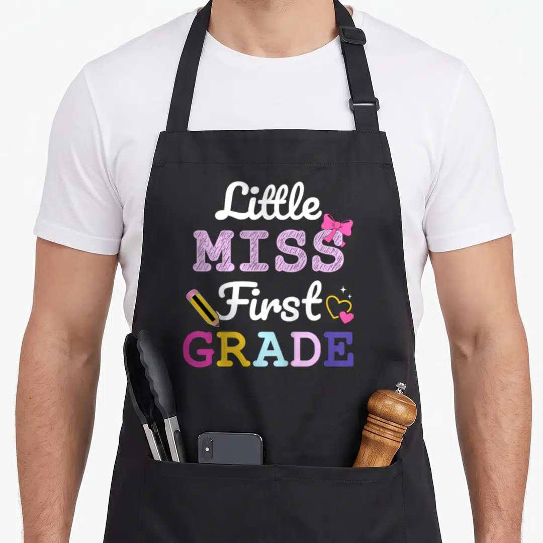 1st school miss grade apron - Little MISS First GRADE text with pink bow, pencil, and hearts in white pink yellow purple — shown on a black cotton canvas apron against a white background