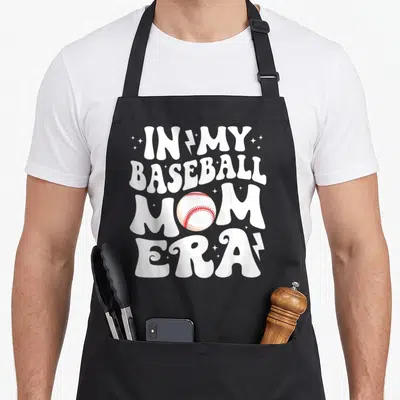 Era baseball apron - Stacked white text reading In My Baseball Mom Era with a red stitched baseball and stars — shown on a black cotton canvas apron against a white background