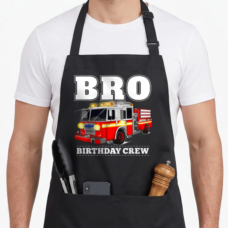 Bro truck apron - Red fire truck with BRO and BIRTHDAY CREW text separated by dashed lines — shown on a black cotton canvas apron against a white background