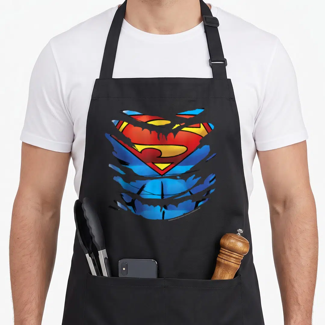 Costume cosplay apron - Superman shield logo tearing through blue fabric in red yellow and black — shown on a black cotton canvas apron against a white background