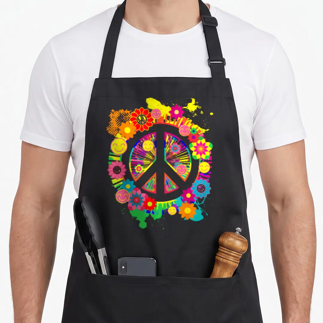 Sign colorful aprons - Multicolored peace sign with flowers and smiley faces on paint splatter background — shown on a black cotton canvas apron against a white background