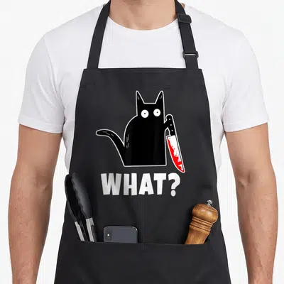 Costume bloody apron - Cartoon black cat holding red bloody knife with white WHAT? text below — shown on a black cotton canvas apron against a white background