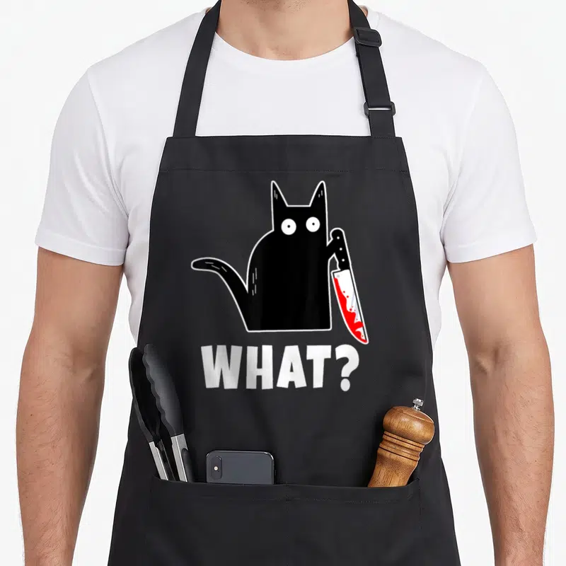 Costume bloody apron - Cartoon black cat holding red bloody knife with white WHAT? text below — shown on a black cotton canvas apron against a white background