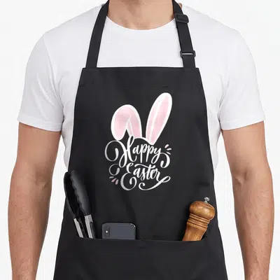 Bunny hunt easter egg apron - Two pink bunny ears above white Happy Easter script with small pink dots — shown on a black cotton canvas apron against a white background
