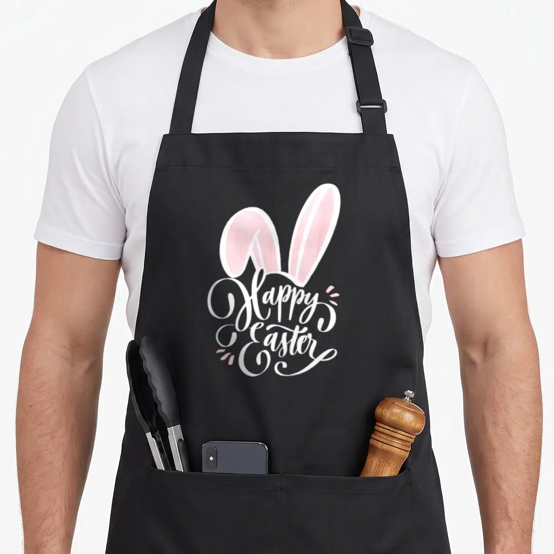 Bunny hunt easter egg apron - Two pink bunny ears above white Happy Easter script with small pink dots — shown on a black cotton canvas apron against a white background