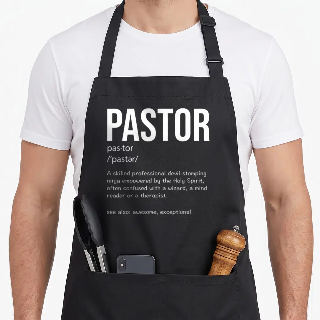 Religious husband wife aprons - White dictionary definition of pastor describing a devil-stomping ninja empowered — shown on a black cotton canvas apron against a white background