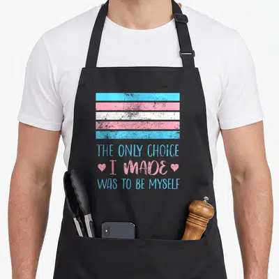 Myself choice aprons - Distressed trans flag with stacked text THE ONLY CHOICE I MADE WAS TO BE MYSELF flanked by two — shown on a black cotton canvas apron against a white background