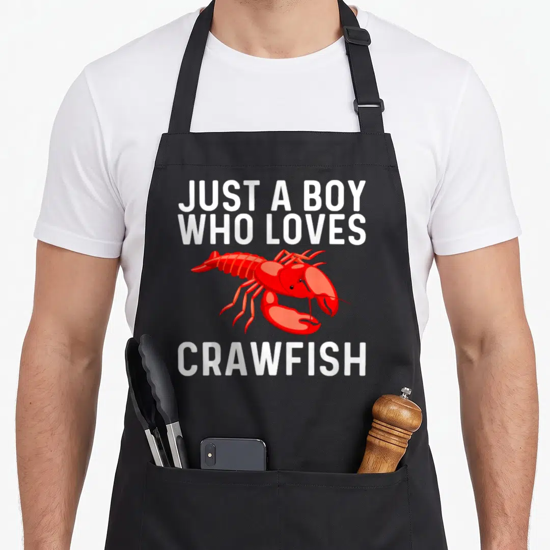 Crawdad lobster apron - Red cartoon crawfish between stacked white text reading just a boy who loves crawfish — shown on a black cotton canvas apron against a white background