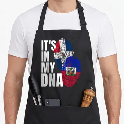 Haitian dominican heritage aprons - IT'S IN MY DNA text next to two overlapping fingerprints filled with Dominican — shown on a black cotton canvas apron against a white background