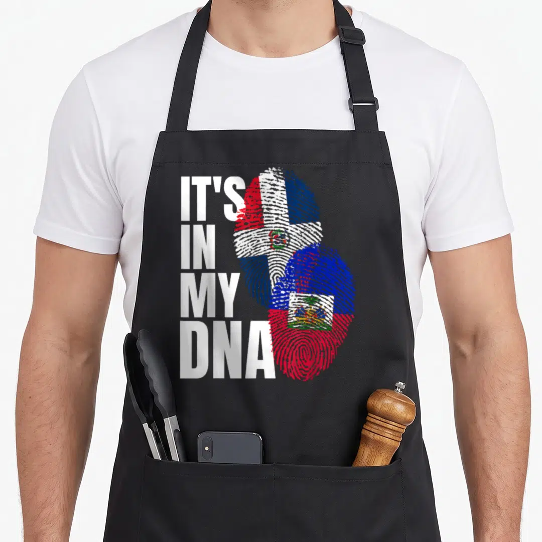 Haitian dominican heritage aprons - IT'S IN MY DNA text next to two overlapping fingerprints filled with Dominican — shown on a black cotton canvas apron against a white background