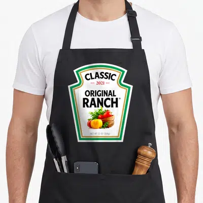 Salad halloween apron - Ranch sauce bottle label graphic with salad bowl and established 2021 text — shown on a black cotton canvas apron against a white background