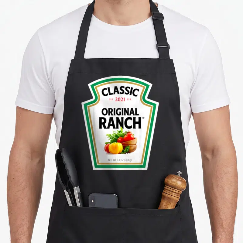 Salad halloween apron - Ranch sauce bottle label graphic with salad bowl and established 2021 text — shown on a black cotton canvas apron against a white background