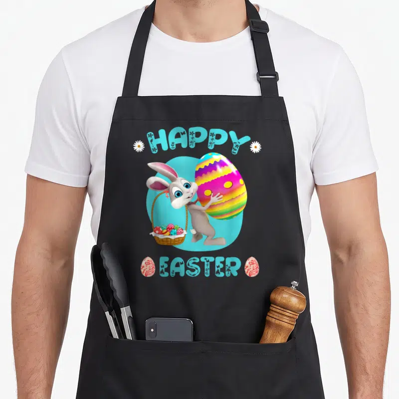 Easter bunny basket apron - Cartoon bunny holding basket and large egg with HAPPY EASTER text in light blue — shown on a black cotton canvas apron against a white background