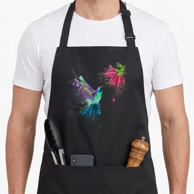 Flower bird apron - Hummingbird flying to pink flower with blue green purple pink watercolor splatters — shown on a black cotton canvas apron against a white background