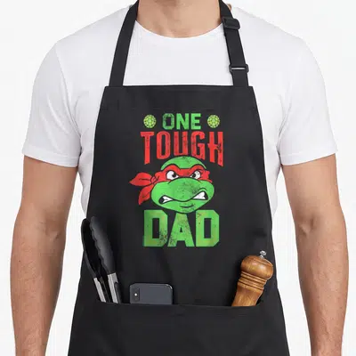 Tough father day apron - Green turtle head red bandana One Tough Dad distressed text — shown on a black cotton canvas apron against a white background