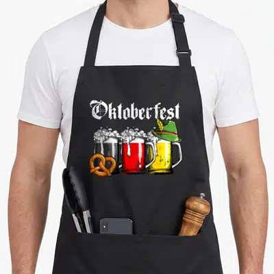 Beer german oktoberfest aprons - Three beer mugs in black red and yellow with a pretzel and green hat under arched — shown on a black cotton canvas apron against a white background